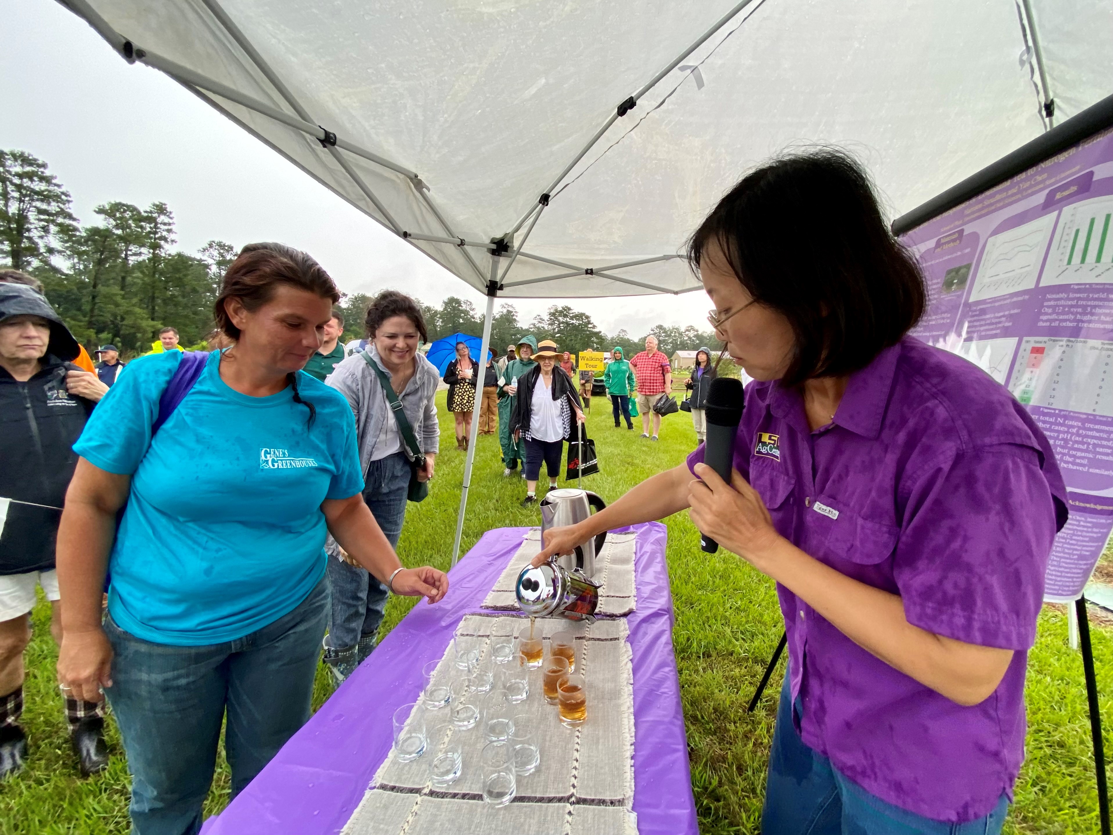 A woman speaking on a microphone pours tea. 